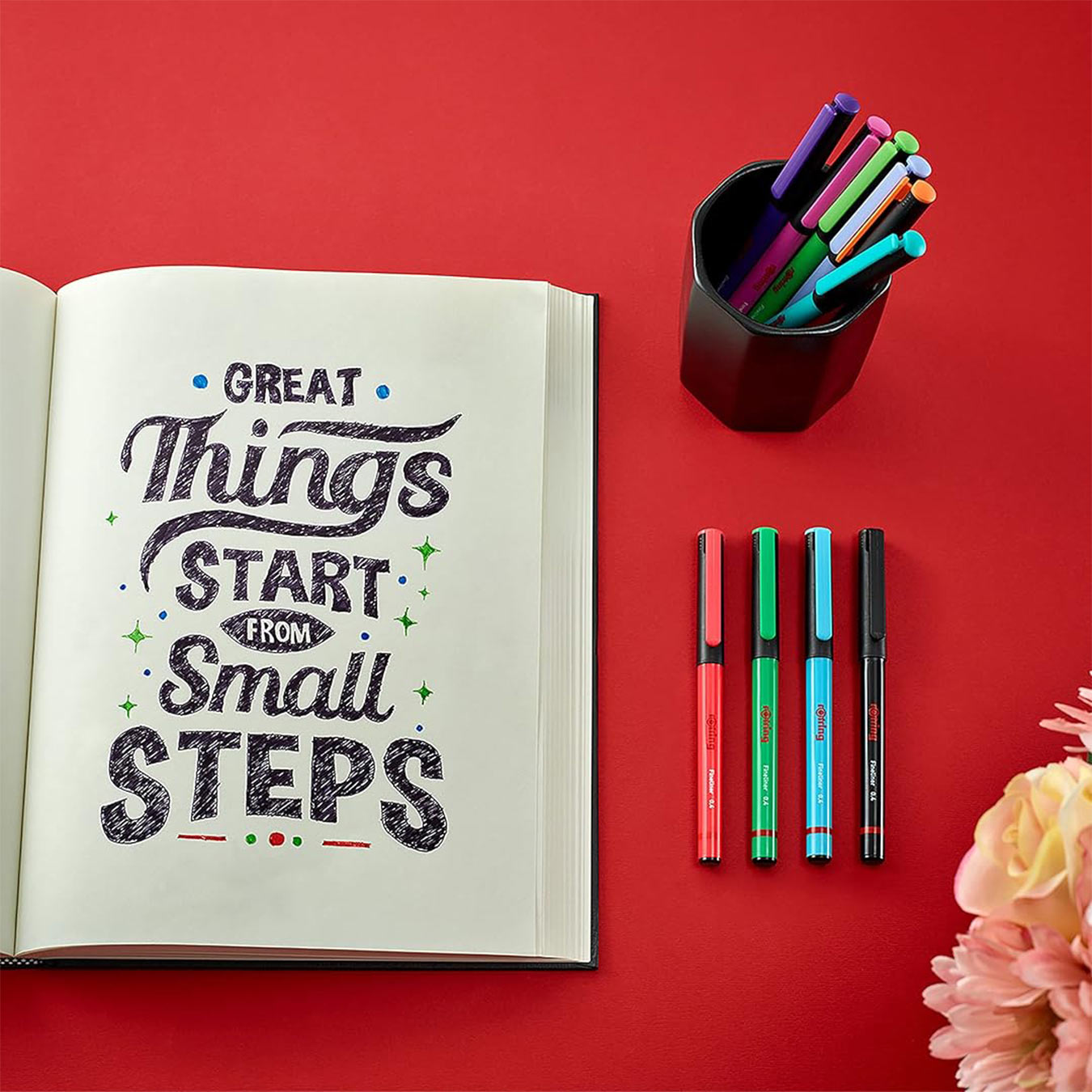 Open notebook with motivational quote, Rotring Liner Fineliner Pens 0.4mm in 4 Assorted Colours, and a flower on a red background
