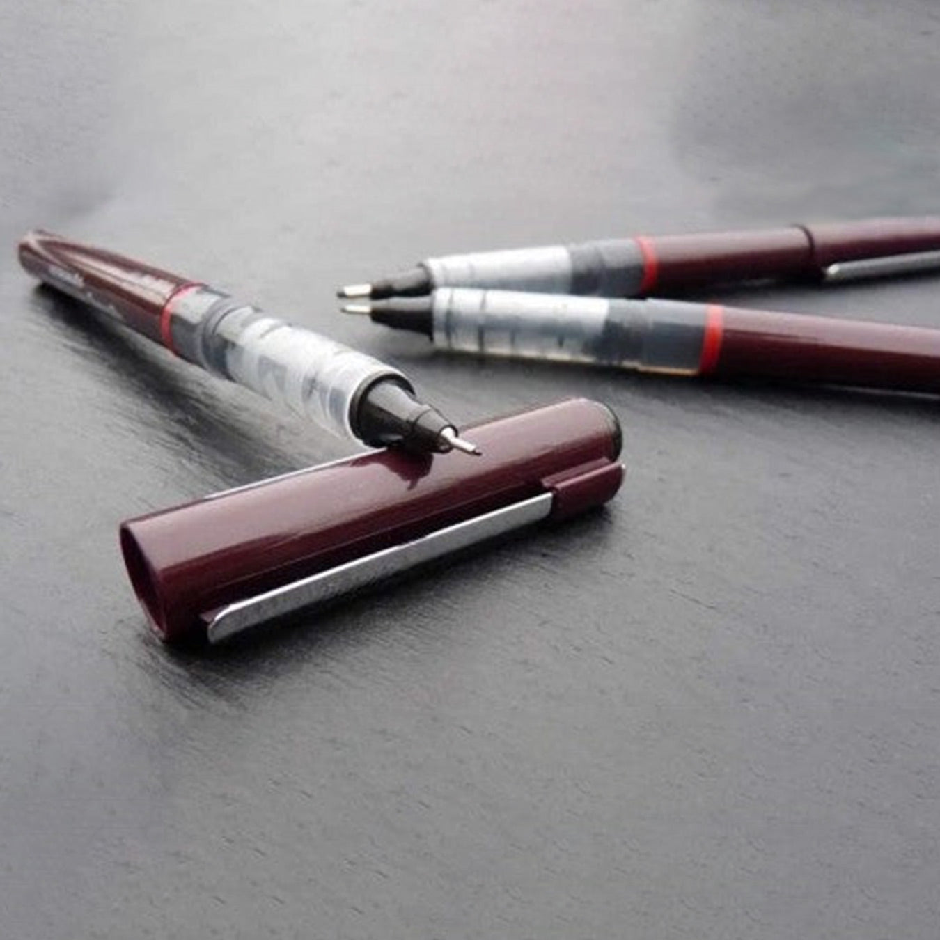 Two pens with burgundy and silver accents on a gray surface