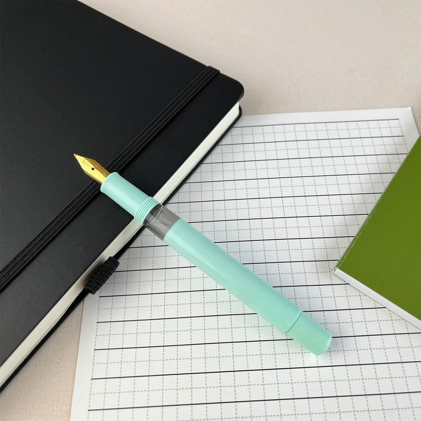 scrikss 419 medium nib Mint green fountain pen on a grid paper with a black notebook and green book in the background.